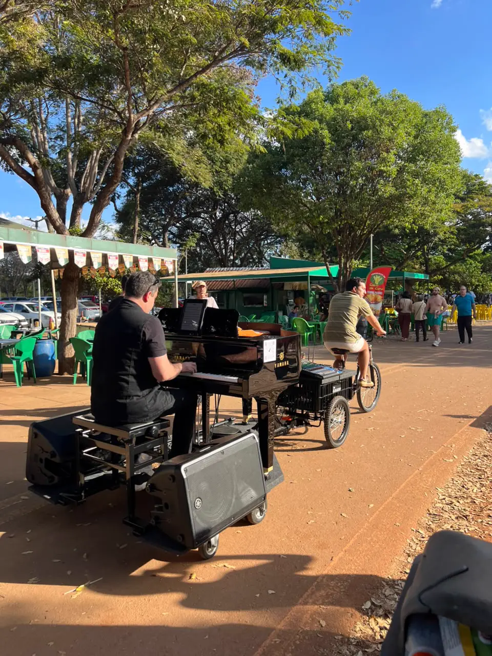 Piano Bike preto em movimento: triciclo rebocando o piano de cauda pelo Parque da Cidade